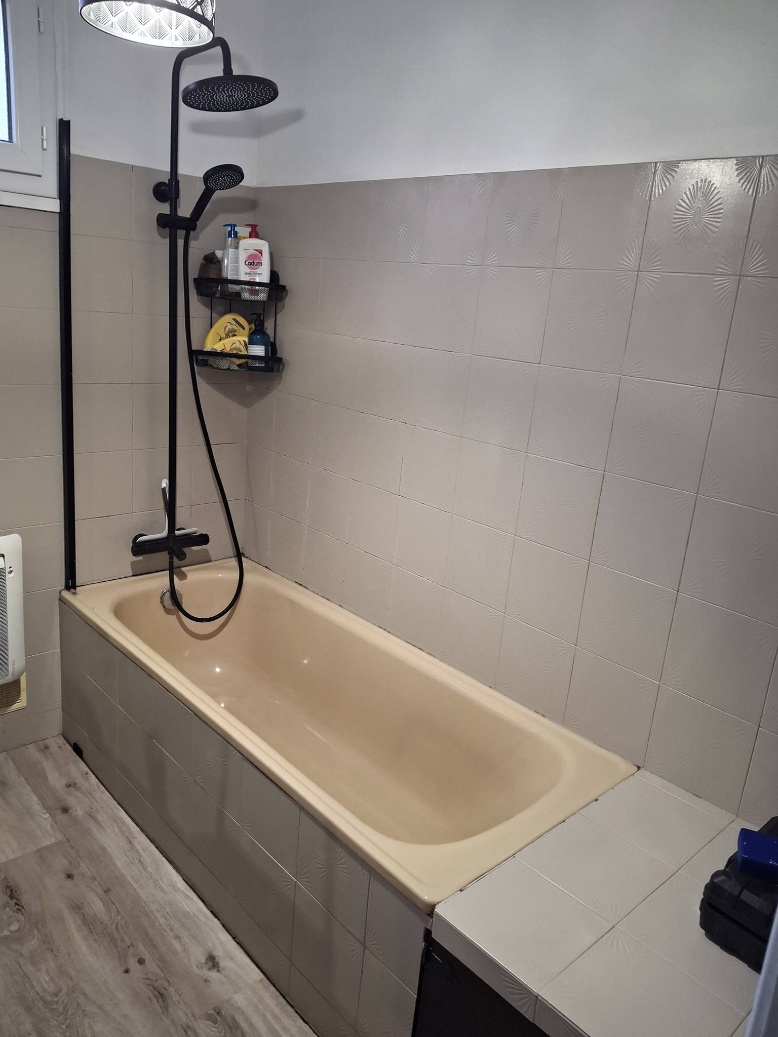 Baignoire beige avec colonne de douche noire et carrelage mural à motifs dans une salle de bain moderne.