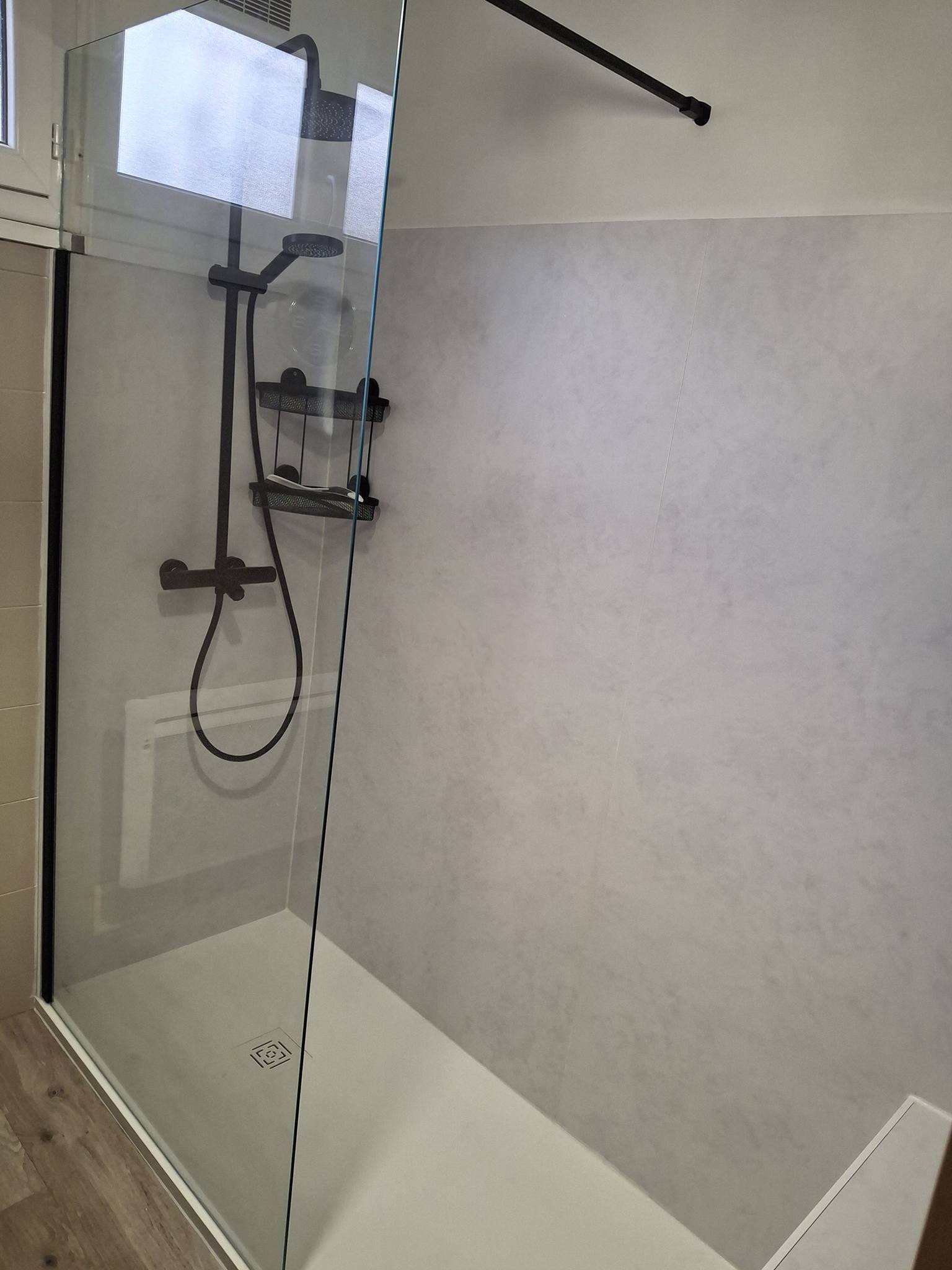 Douche à l'italienne avec robinetterie noire mate, panneaux muraux gris clair marbrés et paroi vitrée.