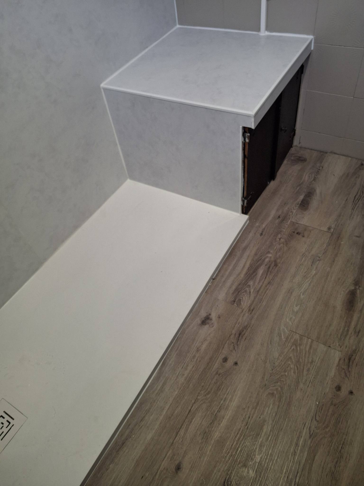 Receveur de douche plat blanc à côté d'un sol en bois et d'un coffrage blanc dans une salle de bain moderne.