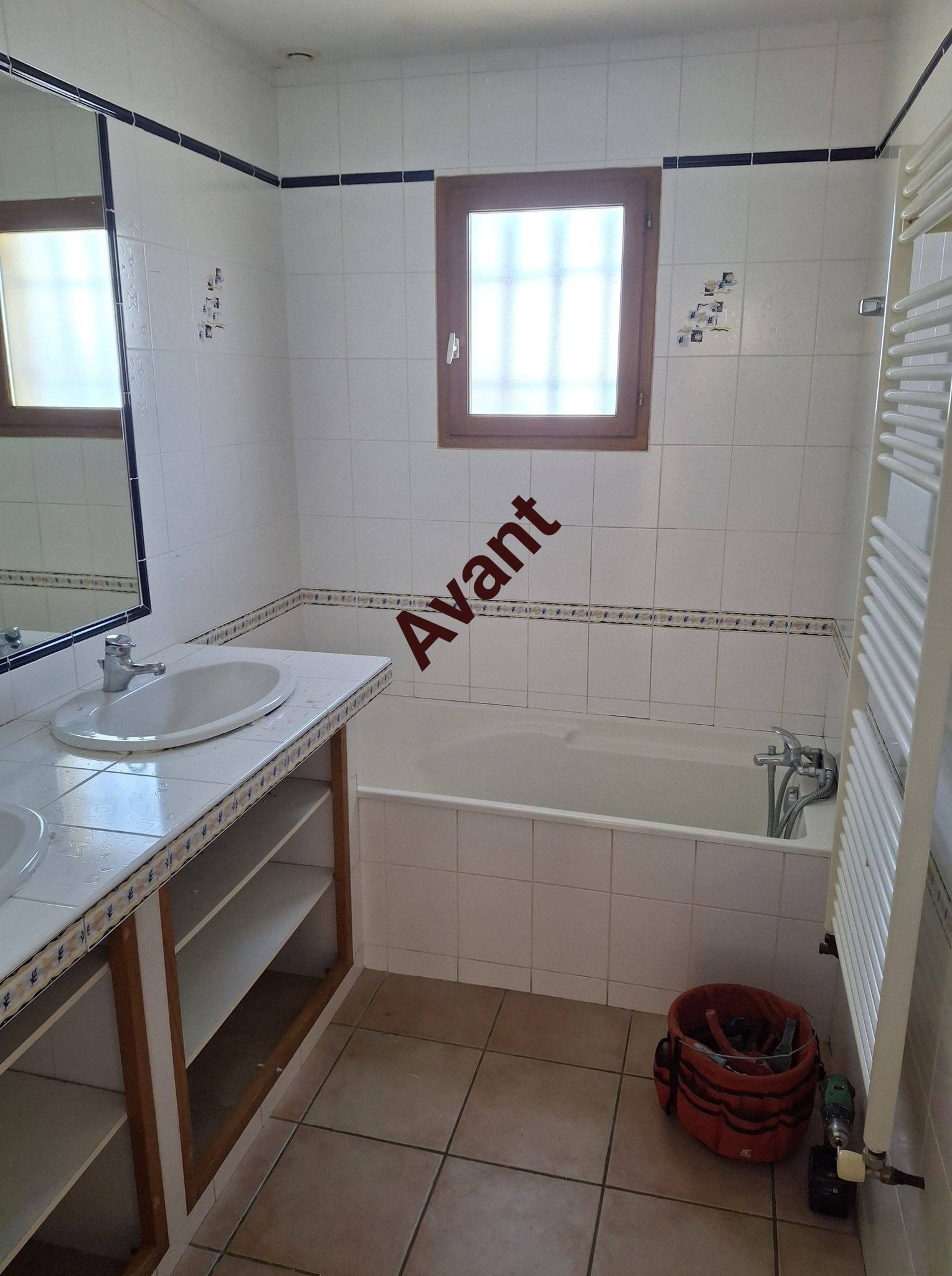 Salle de bain carrelée blanche avec baignoire, lavabo et texte Avant. État d'origine avant projet de rénovation.