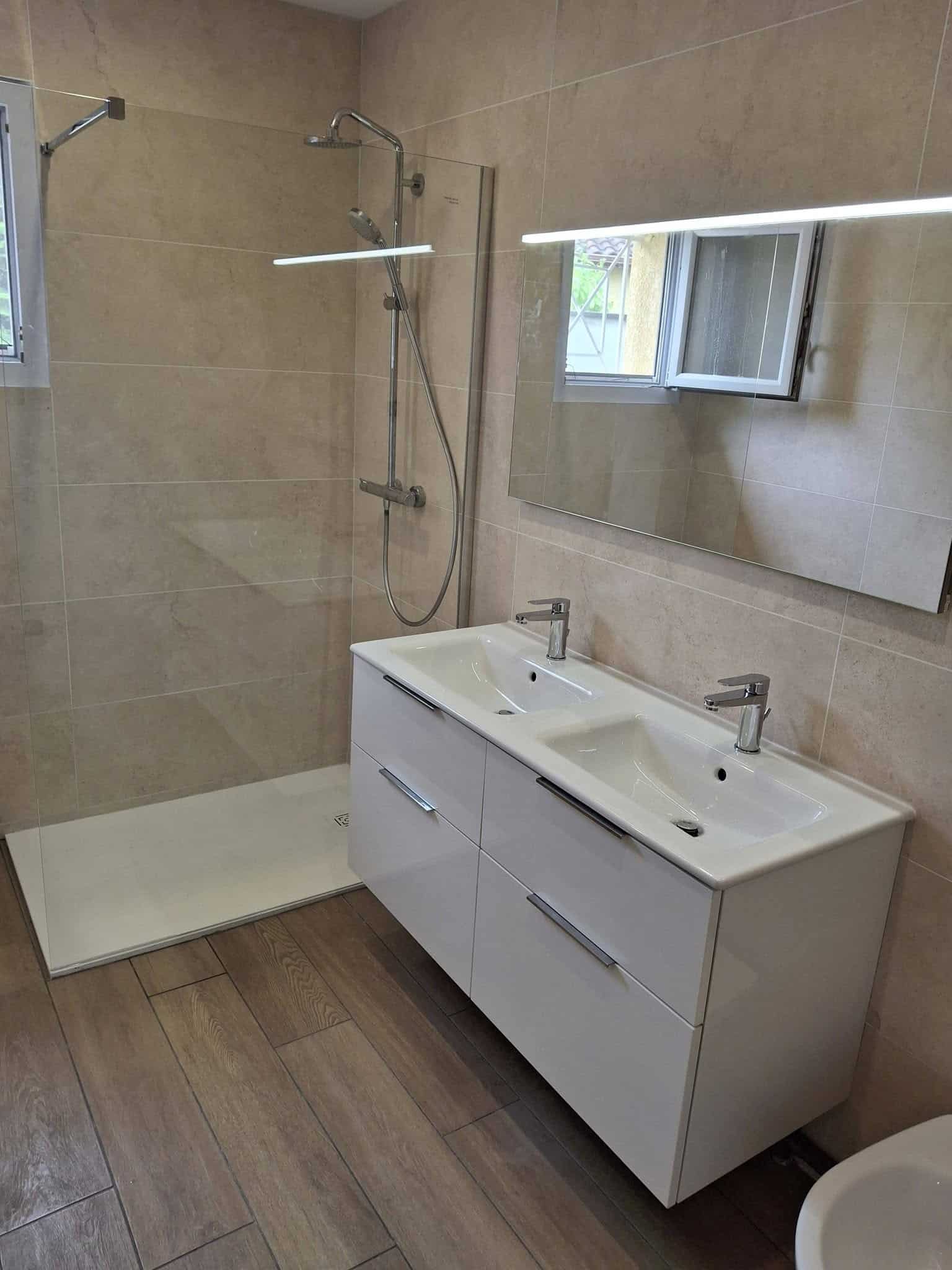 Salle de bain moderne avec douche à l'italienne, double vasque blanche et carrelage beige effet pierre.